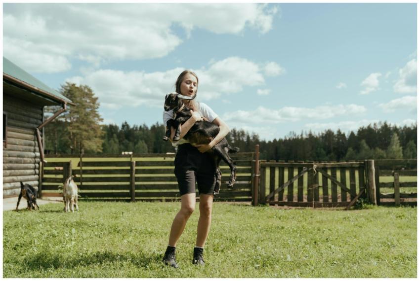 A young woman cuddles a goat outdoors on a sunny d