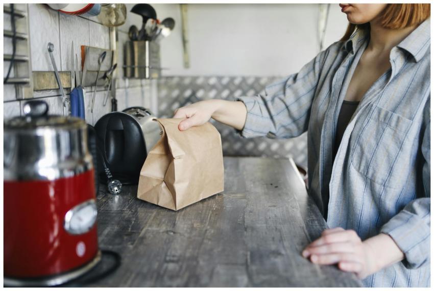Woman in kitchen placing a brown paper bag of food