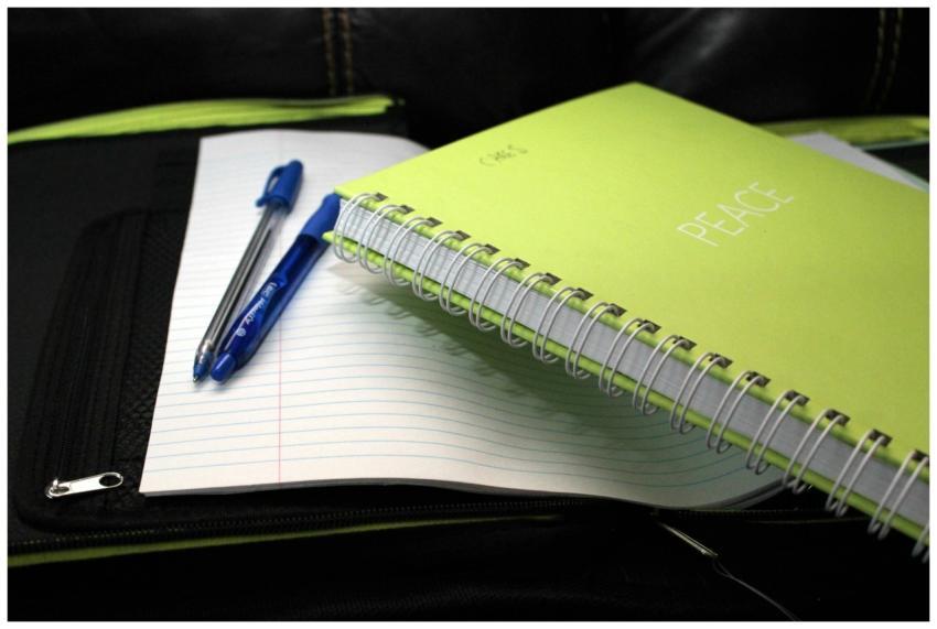 Green spiral notebook labeled 'PEACE' with pens on