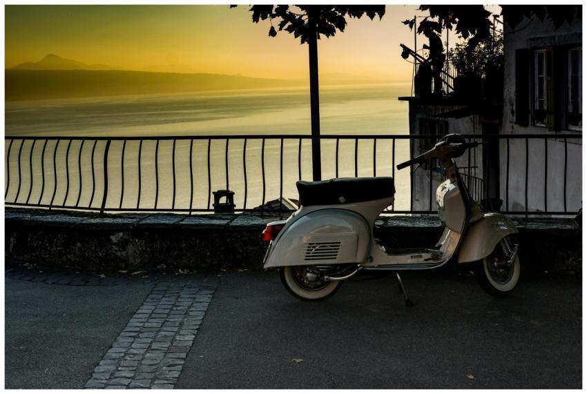 A classic scooter is parked by a scenic railing wi