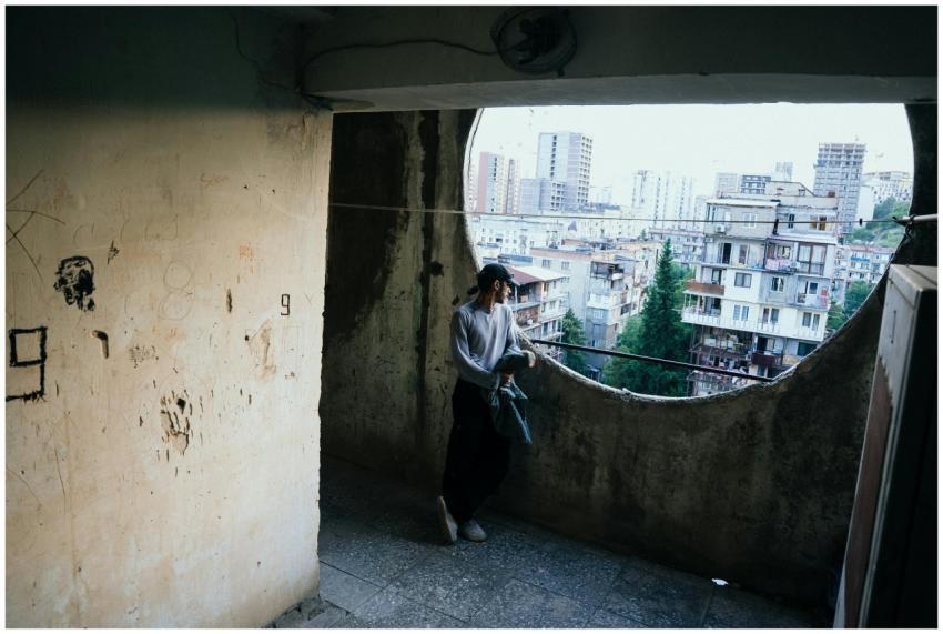 A person stands on a rustic balcony overlooking T'
