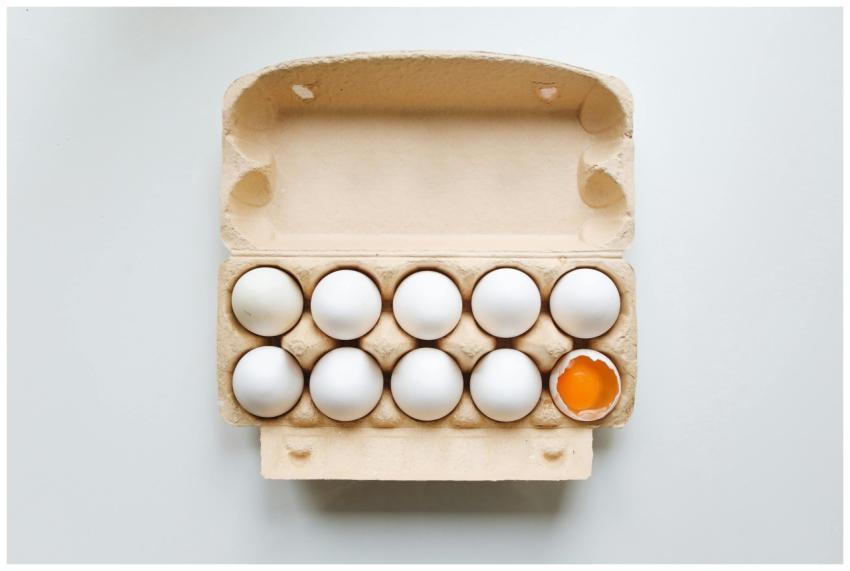 An open egg carton displaying eggs with one broken