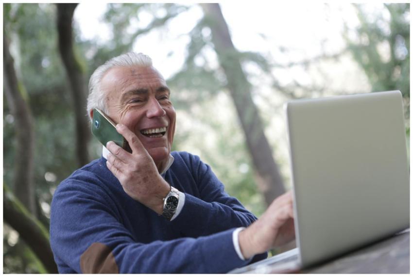 Happy senior man talking on phone and using laptop