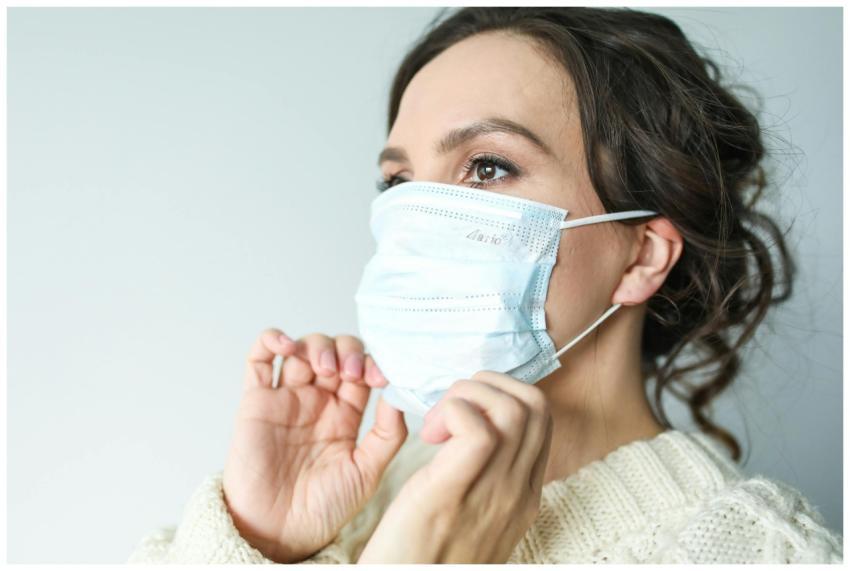 Adult woman adjusting blue surgical mask indoors f