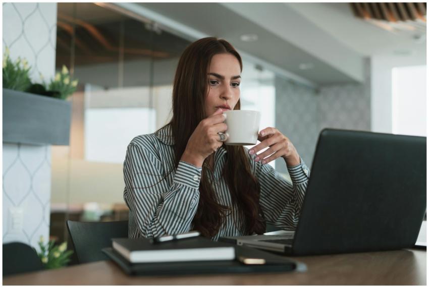 Young woman drinking coffee while working on lapto