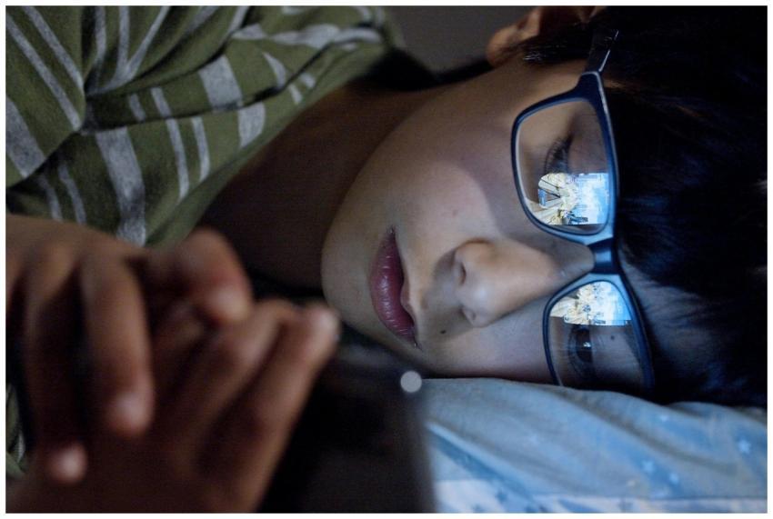 A child lying in bed at night using a smartphone,