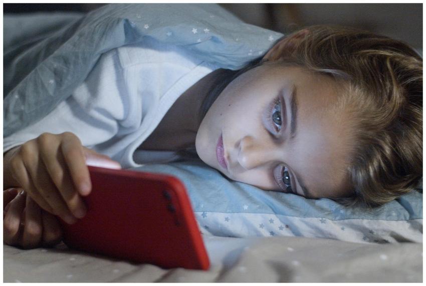 Child lying in bed under a blanket, focused on a s