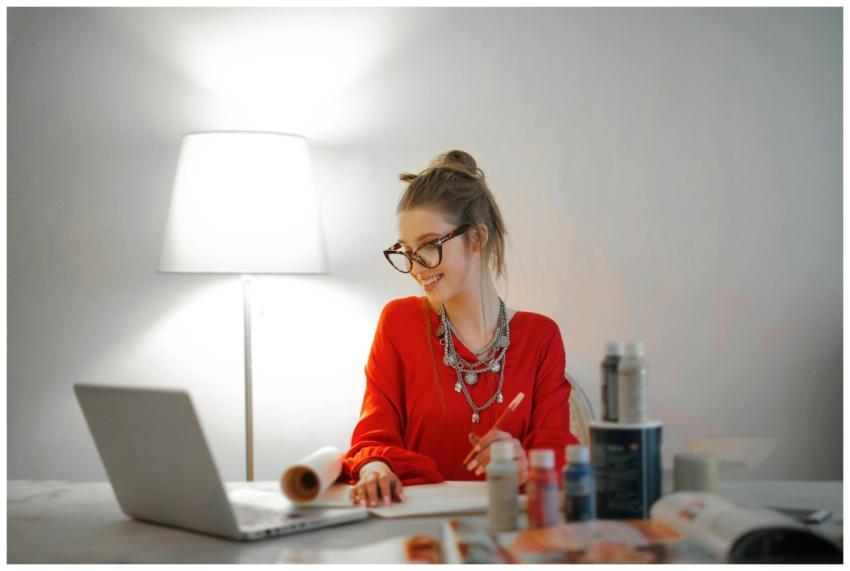 Smiling woman in red using laptop and art supplies