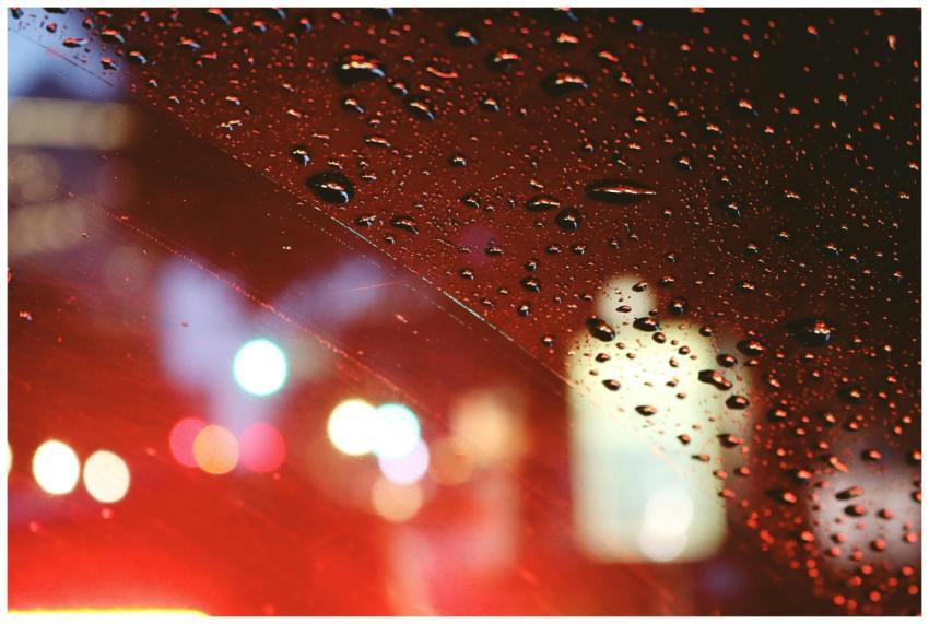 Blurred city lights through raindrop-covered car w