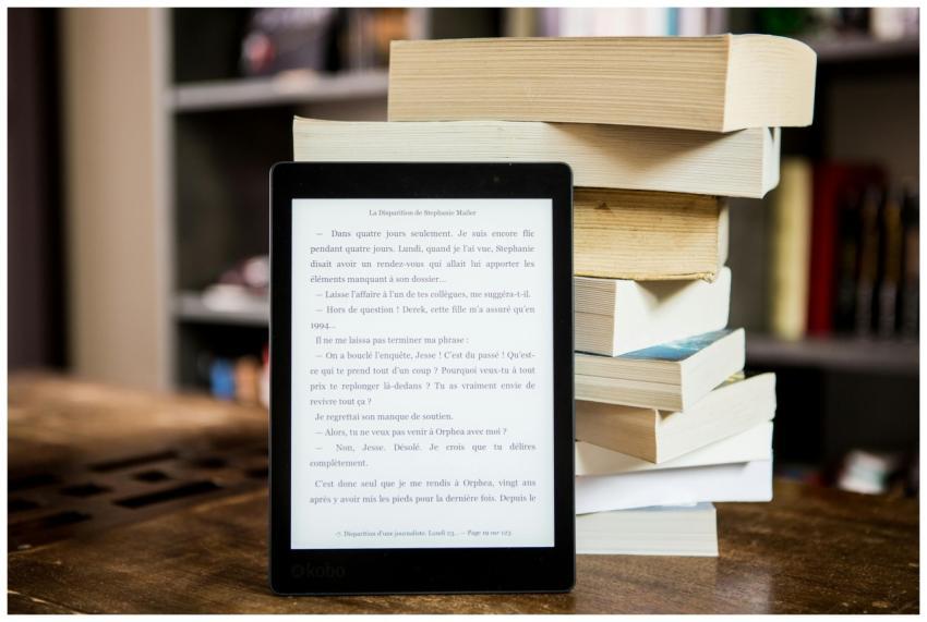 E-reader with text displayed next to a stack of ph