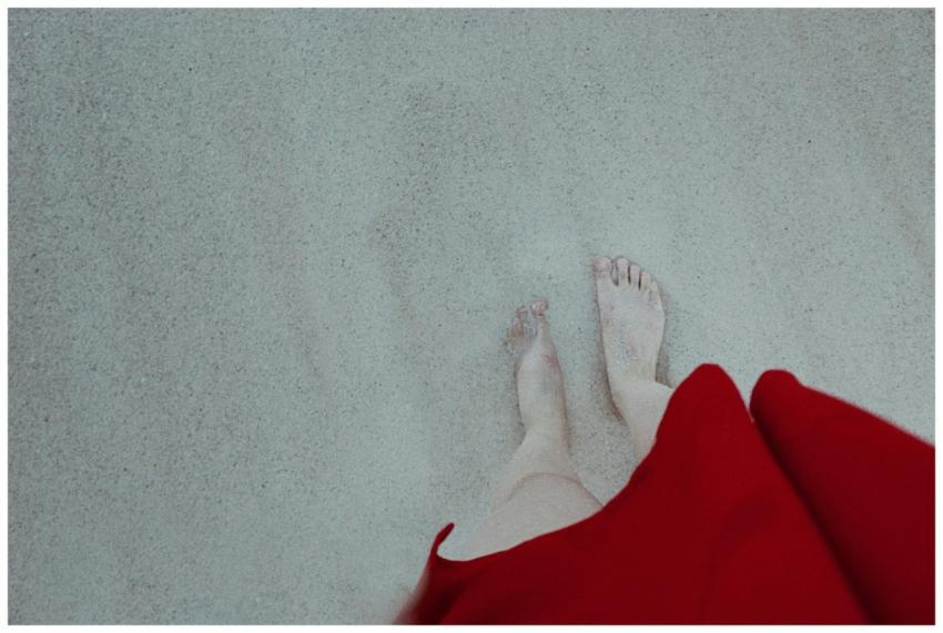 Barefoot woman in red dress standing on sandy beac