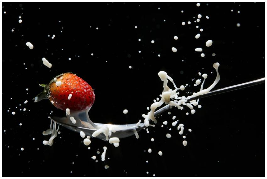 A strawberry captured in motion with milk splashin