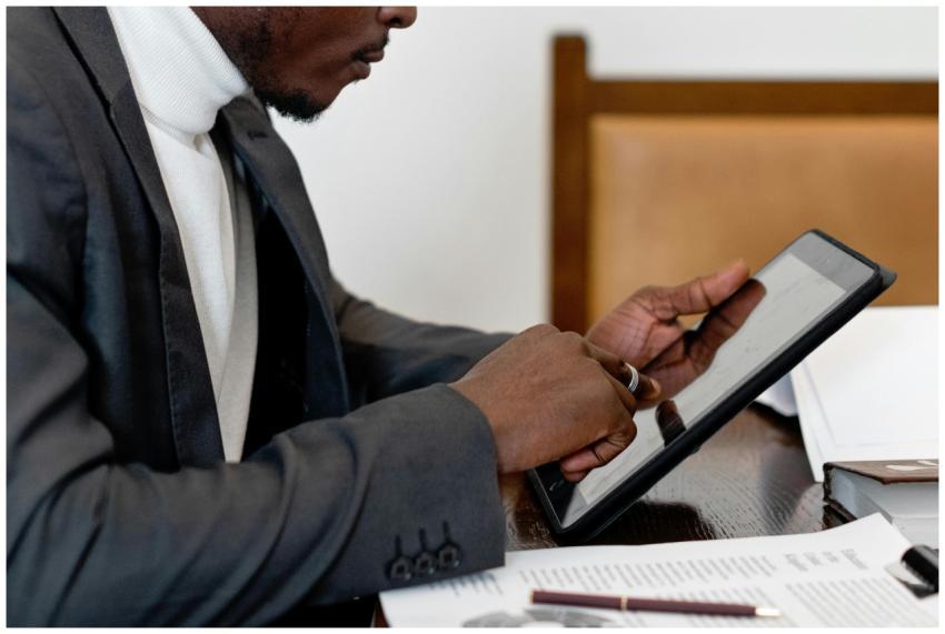 A businessman in a suit uses a tablet at a desk, f