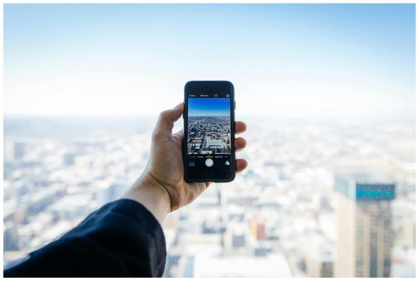 A hand holding a smartphone capturing an urban cit