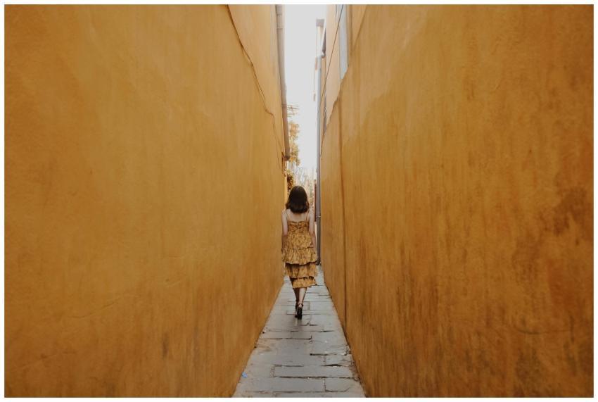 A woman in a yellow dress walks through a narrow a