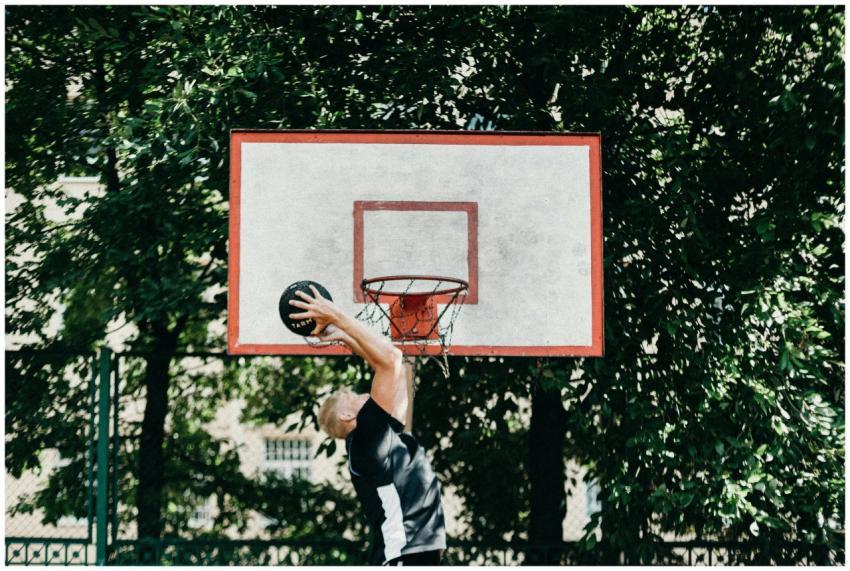 A man performing a slam dunk on an outdoor basketb