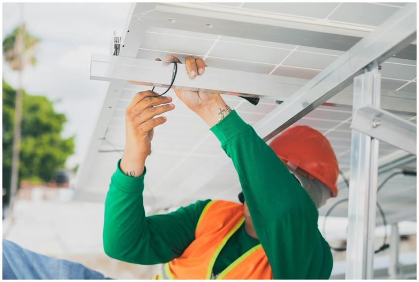 A solar technician in PPE installs a solar panel,