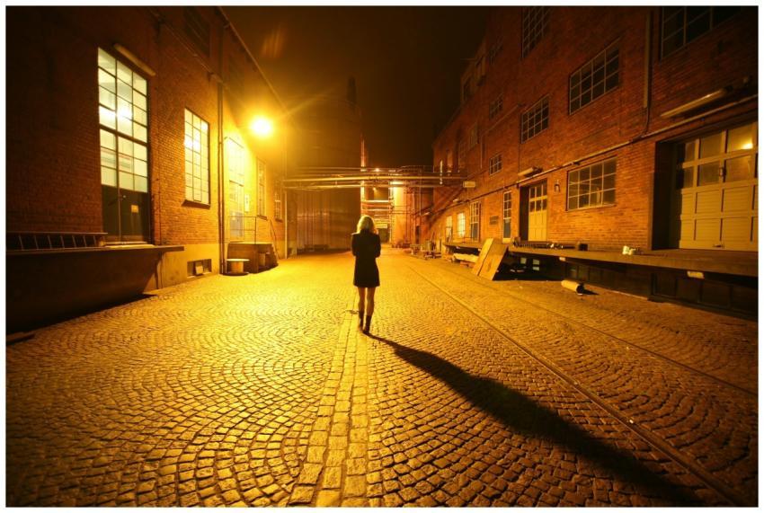 A woman walks alone down a cobblestone alley illum