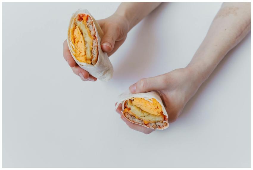 Close-up of hands holding a cut breakfast burrito
