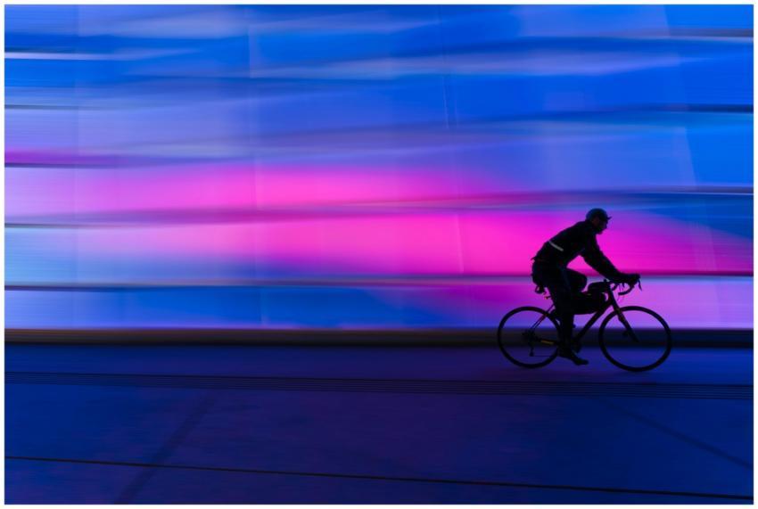 A cyclist's silhouette zooms past a colorful urban