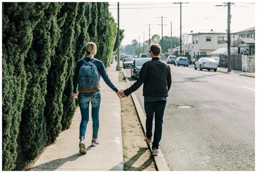 A couple walks hand in hand along a sunny sidewalk