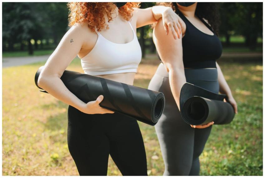 Two women in activewear holding yoga mats together