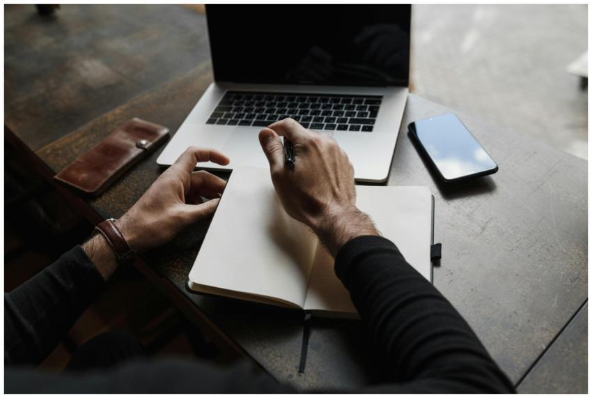 Overhead view of hands writing in a notebook besid