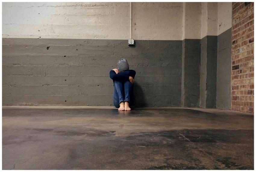 Person sitting in an empty room against a concrete