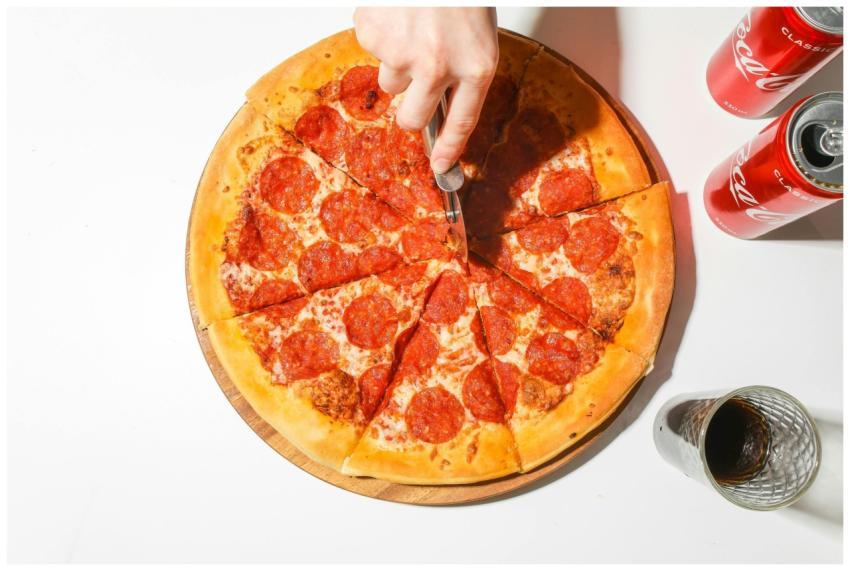 A delicious pepperoni pizza being sliced with clas