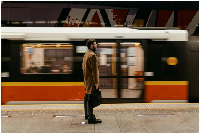 A man in a coat holding a briefcase stands at a tr