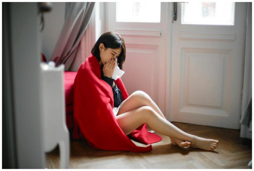 A woman sits on the floor indoors, wrapped in a re
