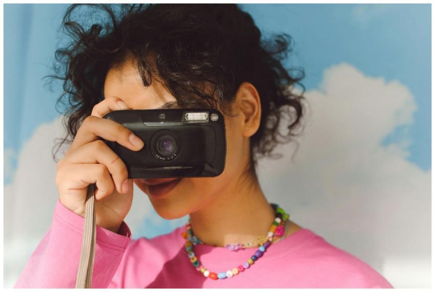 A young woman with curly hair holds a retro camera