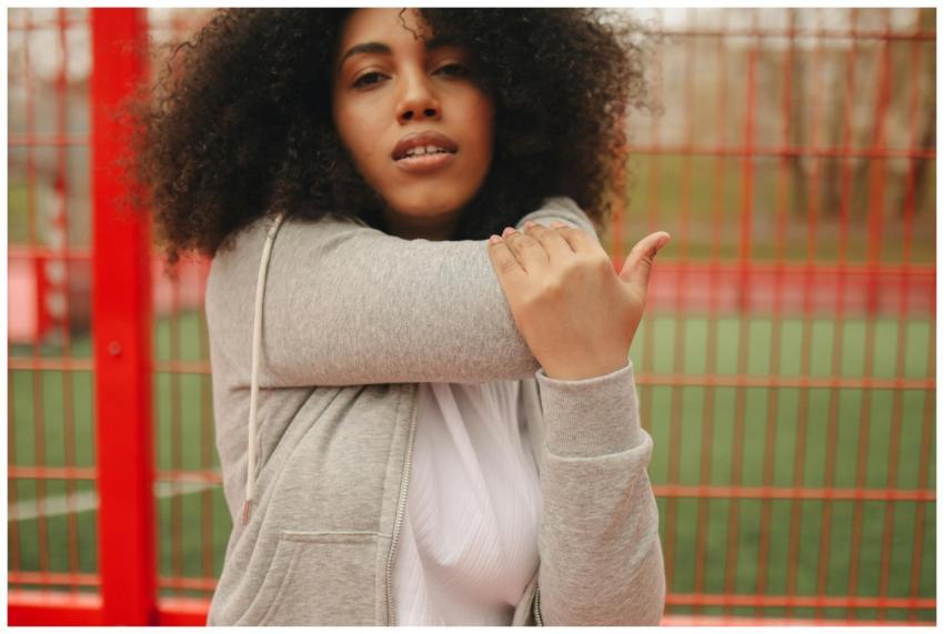 A young woman with curly hair stretches outdoors n