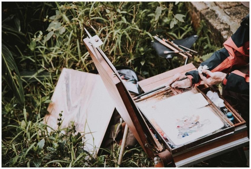 An artist painting outdoors with a wooden easel an