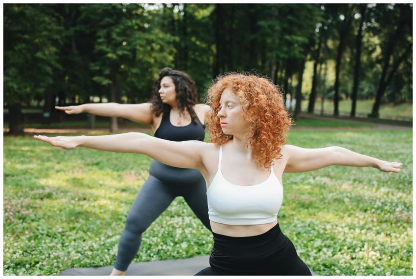 Two women perform yoga poses in a green outdoor pa