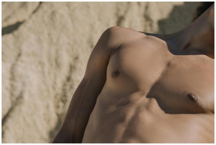 Close-up of a shirtless man's torso with a sandy b
