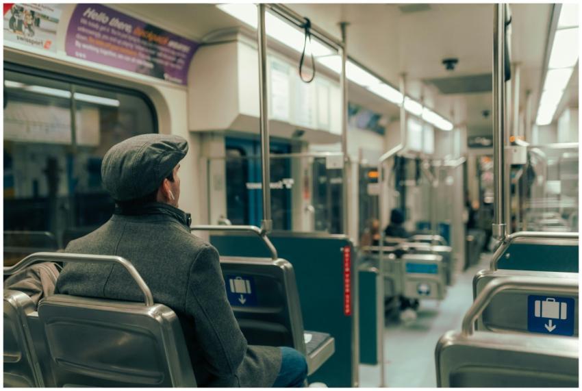 A man in a cap and coat sits inside a modern subwa
