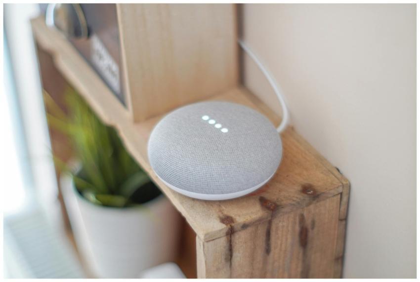 A Google Home Mini smart speaker on a wooden shelf