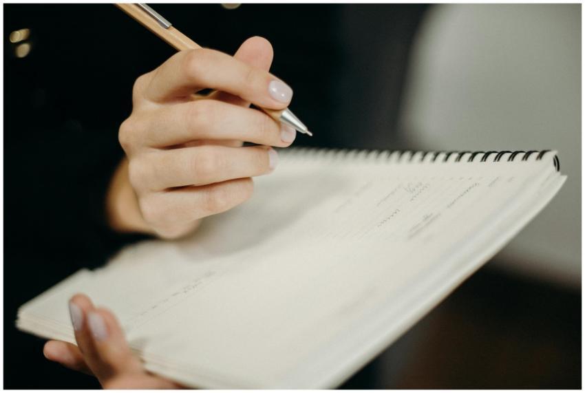 A person's hand holding a pen writing in a spiral