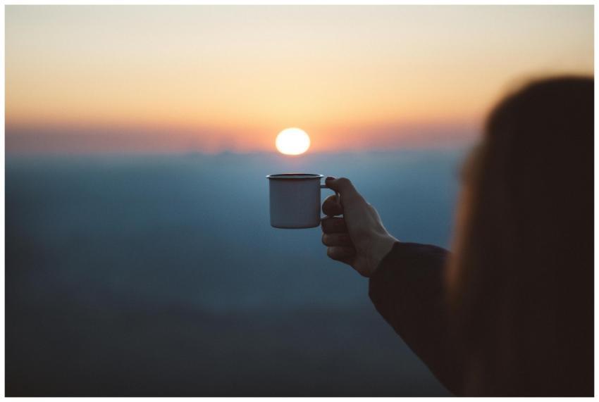 A person holds a coffee cup against a beautiful su
