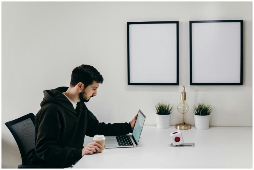 Young man in a hoodie works on a laptop in a moder