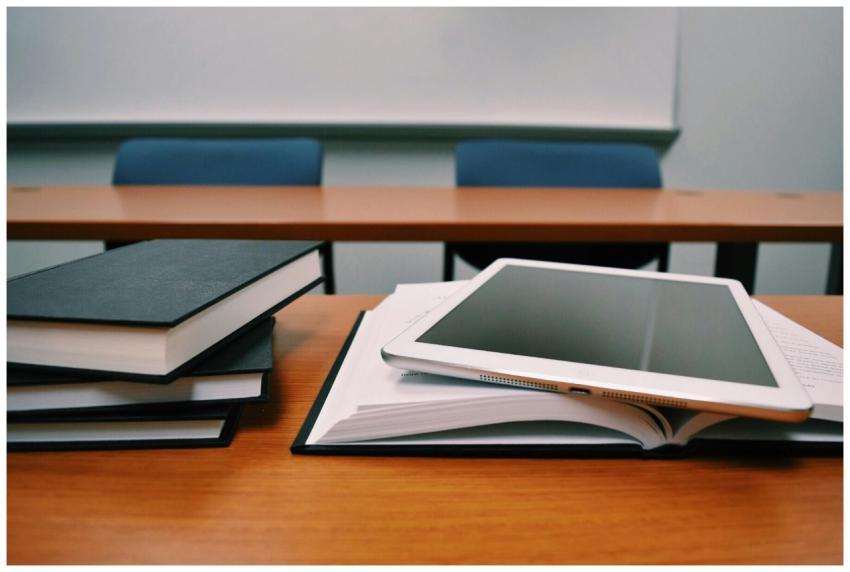 Books and a tablet on a desk in a classroom, depic