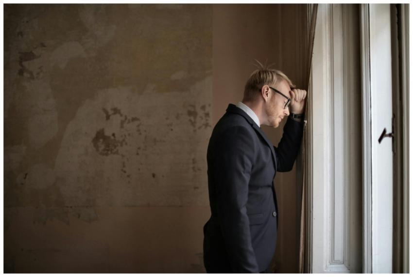 A worried businessman in a suit leaning against a