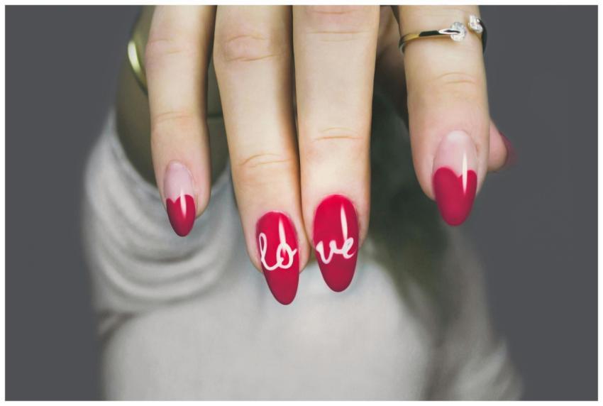 Vibrant red nails with 'love' art on a woman's han