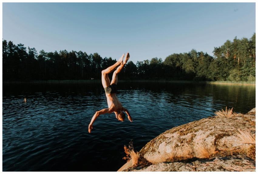 A man performing a dive from a rock into a scenic