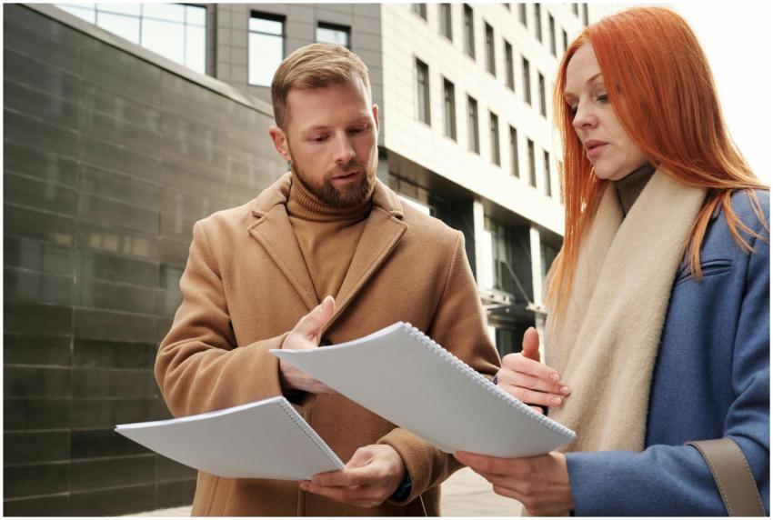 Two business professionals in coats discuss docume