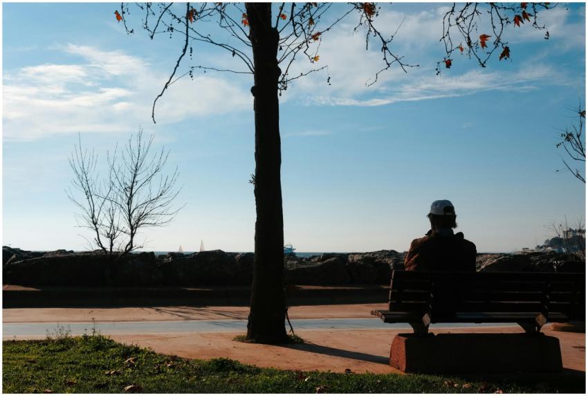 An individual sitting alone on a bench by the sea,