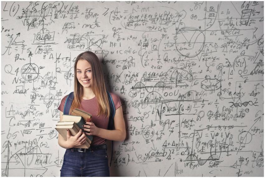 Young woman holding books standing in front of a c