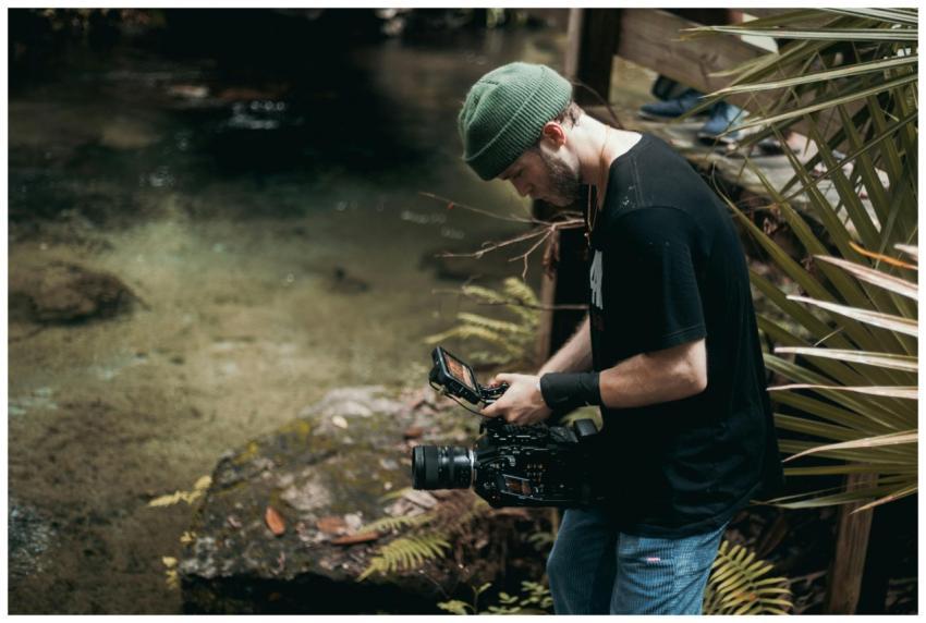 A bearded man in a beanie operates a video camera