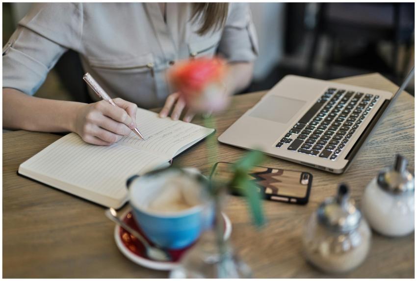 Woman writing in a notebook with a laptop and coff
